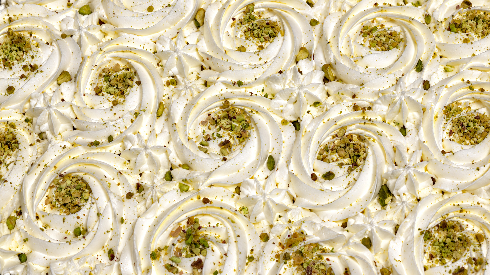Piped cream rosettes with pistachio dust across a milk cake sharing tray